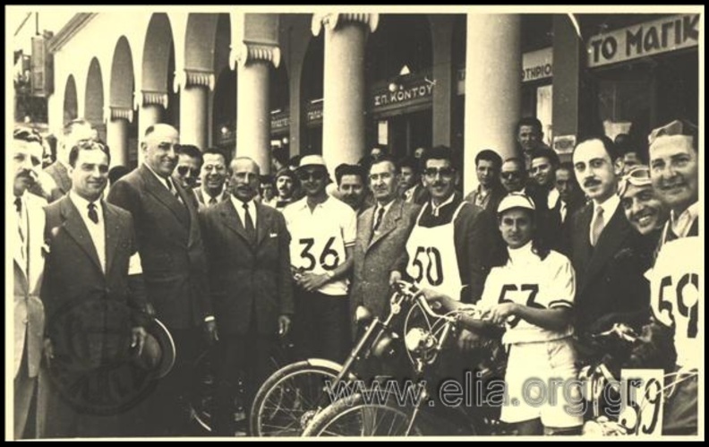 12. Εκκίνηση των μοτοσυκλετικών αγώνων Πατρών - Αθηνών, 1954 (φωτό Νιλόλαος Μπούρης), πίσω διακρίνονται τα μαγαζιά στον ΕΣΠΕΡΟ, επίσης βλέπουμε και μία μοτοσυκλετίστρια.JPG