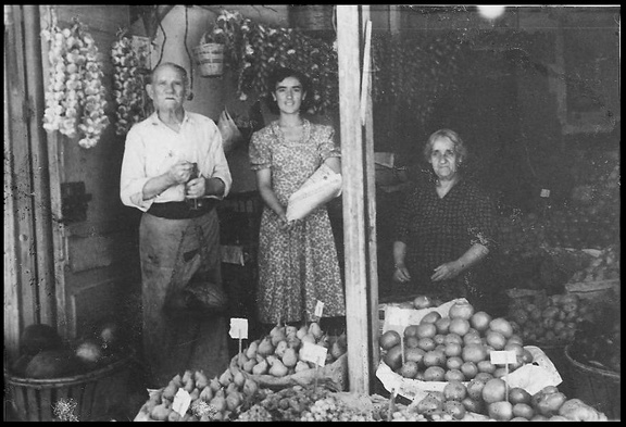 25. Μανάβικο Κορίνθου &ι Κανάρη (1929-1956). Έκλεισε αναγκαστικά γιατί στη θέση του κτίστηκε το ΙΚΑ. Στη φωτογραφία ο Γεράσιμος Σπυρόπουλος με τη κόρη του Τούλα και τη σύζυγό του Βιργινία, 1950